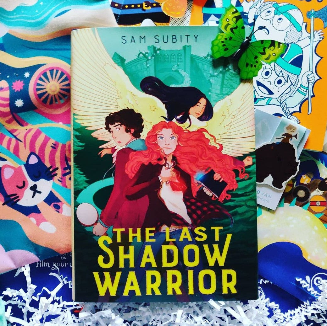 Book cover shows a white girl with red hair centered, a white boy with dark hair to her left, and an Asian American girl with black hair and yellow wings above the two others. Cover is mostly green with a castle in the background.