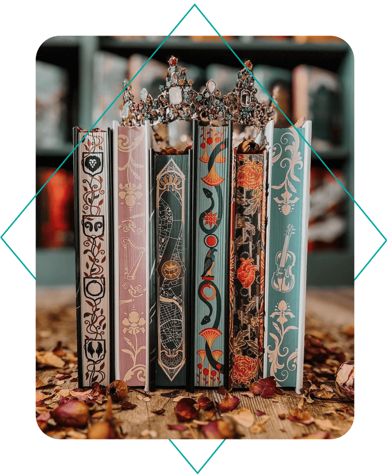 A row of books of different sizes with a crown placed on top, set on a table. Each book has stenciled edges.